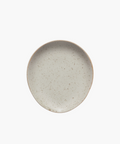 Simple round ceramic spoon rest with a smooth, light beige surface and subtle dark speckles. It conveys an earthy and minimalist aesthetic. | Wildwood Home Co.