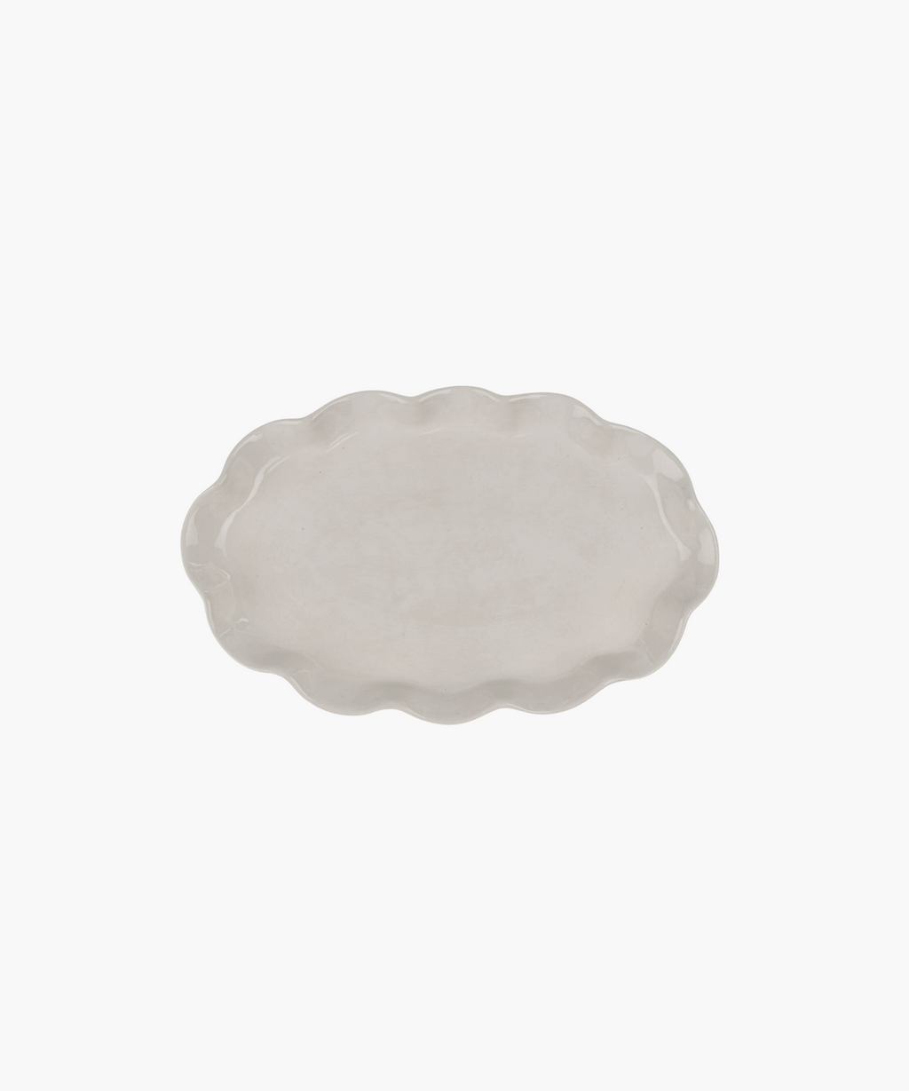 An oval, ceramic platter with a wavy, scalloped edge in a light cream color. The minimalist design conveys simplicity and elegance. | Wildwood Home Co.