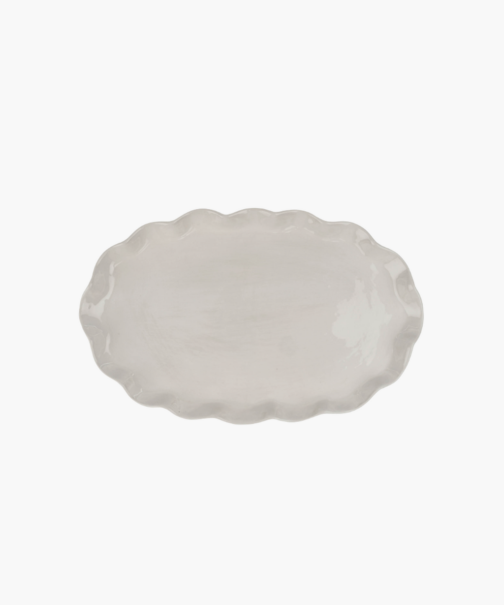 An oval, ceramic platter with a wavy, scalloped edge in a light cream color. The minimalist design conveys simplicity and elegance. | Wildwood Home Co.