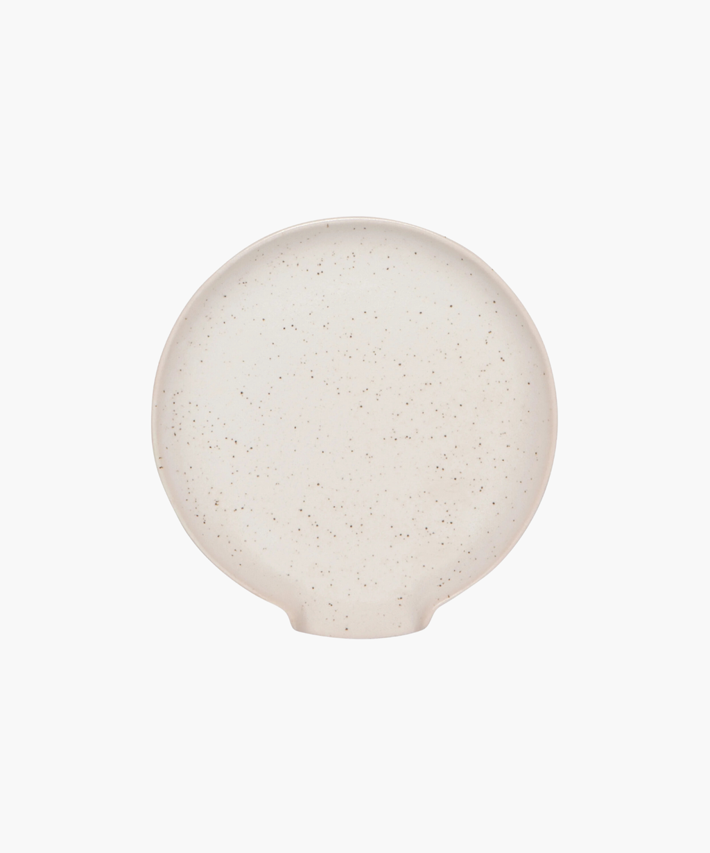 Overhead view of a round, beige ceramic spoon rest with a slightly raised rim and subtle speckled texture on a white background. The tone is simple and minimalist. | Wildwood Home Co.