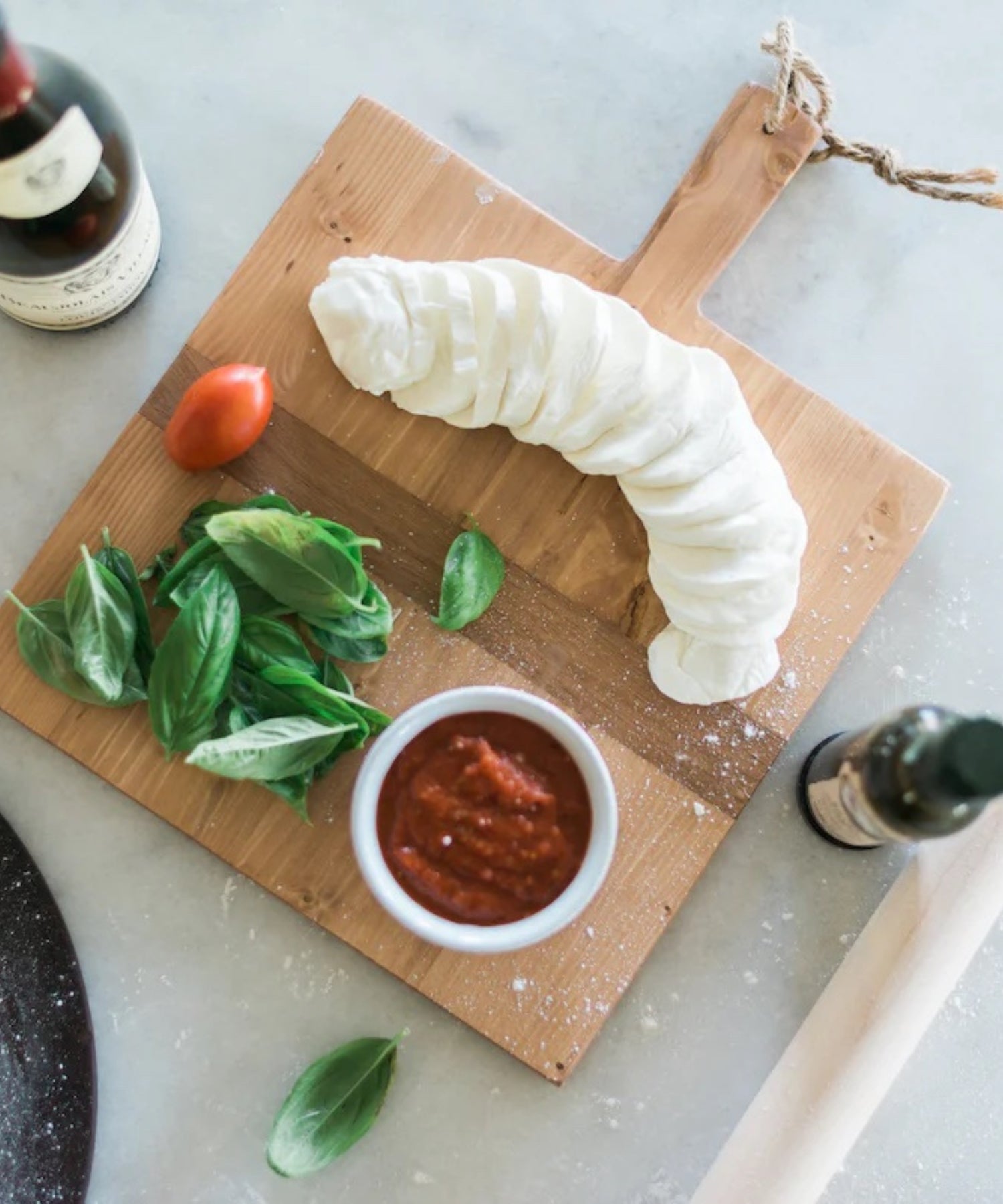 Square pine wood cutting or charcuterie board with a natural finish, featuring a dark horizontal stripe and a handle with a rope loop styled with cheese and wine.  | SW Home