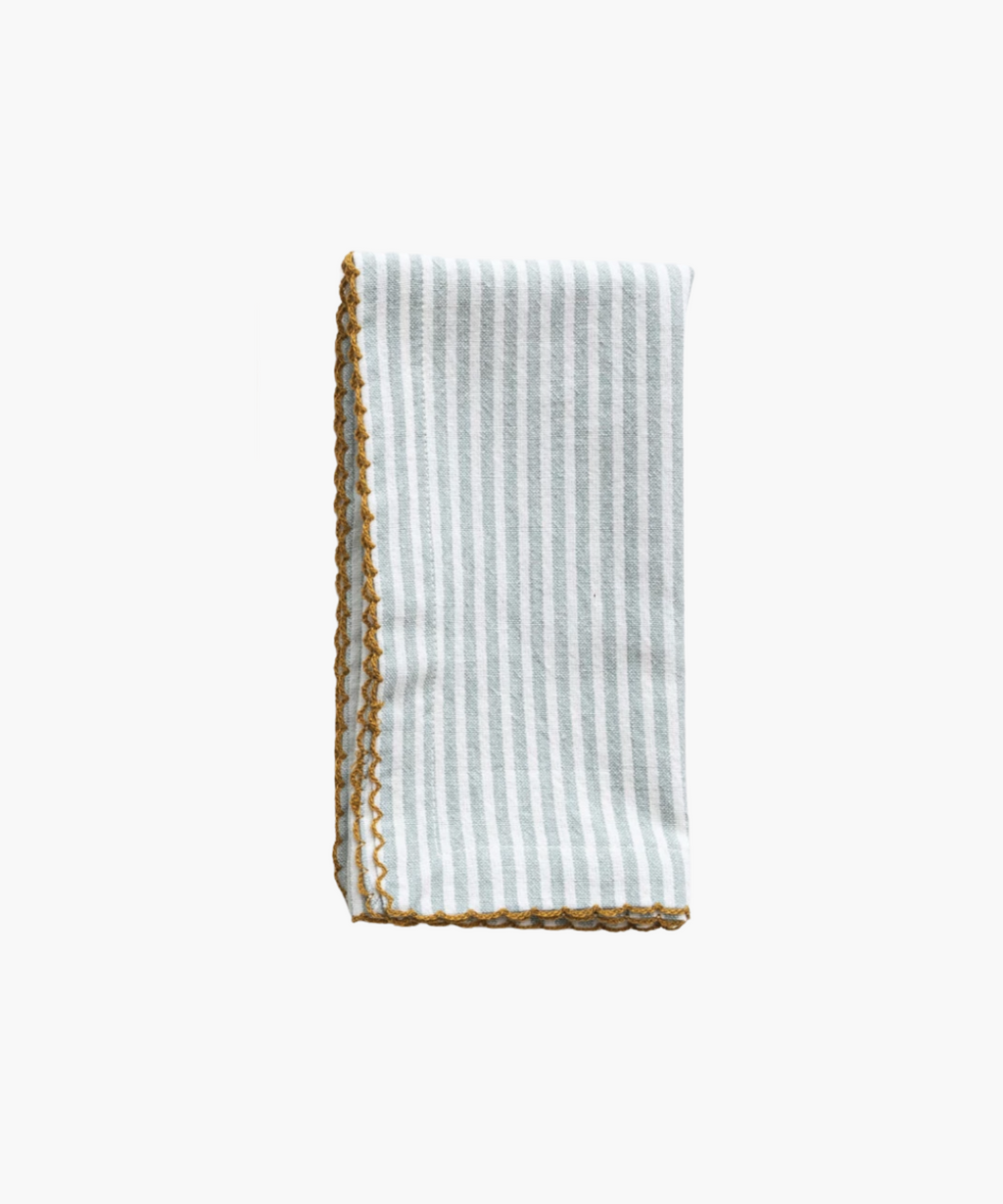 A folded napkin with pale blue vertical stripes and a decorative yellow scalloped edge. The design is simple, evoking a clean, elegant feel. | Wildwood Home Co.