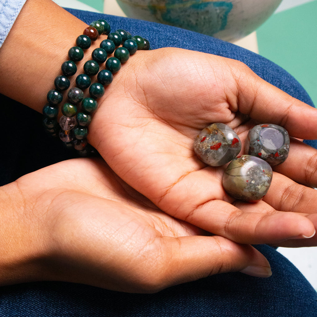 Biracial woman wearing 3 genuine Bloodstone crystal bracelets and holding 3 Bloodstone crystals in her upturned open palm by Energy Muse