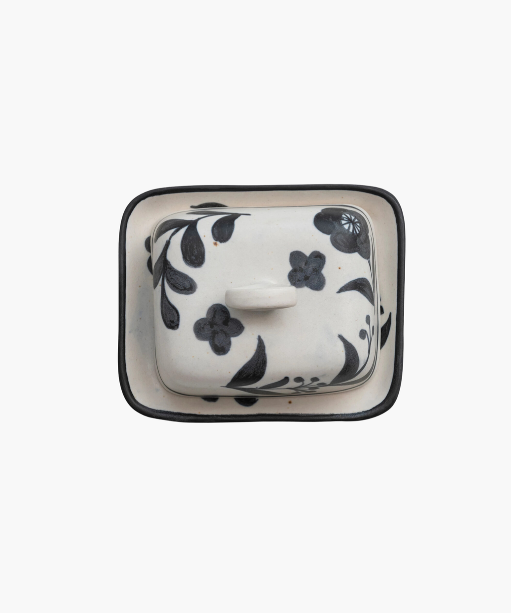An overhead picture of a ceramic butter dish with a lid featuring black floral designs and a circular handle, set against a plain white background. The tone is elegant and artistic. | Wildwood Home Co.